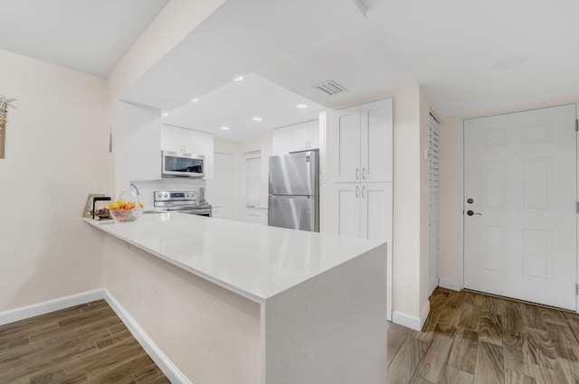 kitchen featuring kitchen peninsula, hardwood / wood-style floors, stainless steel appliances, and white cabinets