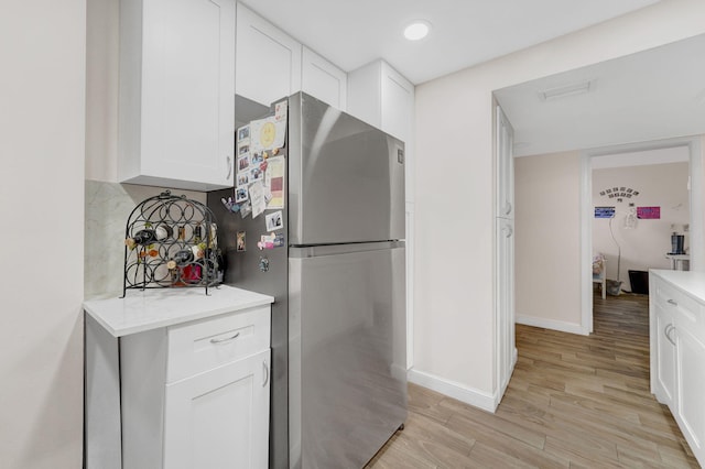 kitchen with stainless steel fridge, backsplash, white cabinets, and light hardwood / wood-style floors