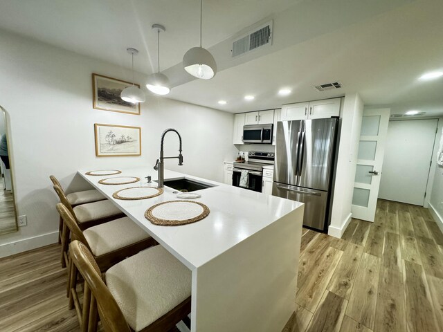 kitchen with light hardwood / wood-style flooring, stainless steel appliances, decorative light fixtures, sink, and white cabinets