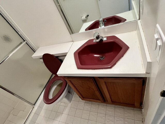 bathroom featuring tile patterned flooring, a shower with shower door, toilet, and vanity