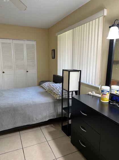 bedroom featuring light tile patterned flooring, ceiling fan, a closet, and a textured ceiling