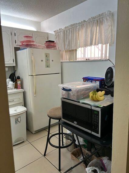 kitchen with a textured ceiling, light tile patterned floors, white cabinets, and white fridge