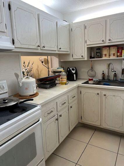 kitchen with a textured ceiling, range hood, sink, electric range, and light tile patterned flooring