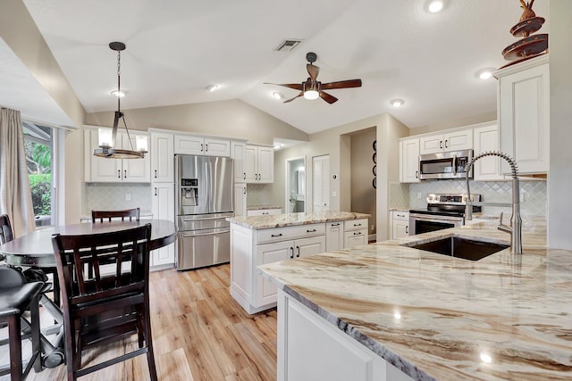 kitchen featuring white cabinets, backsplash, appliances with stainless steel finishes, vaulted ceiling, and decorative light fixtures