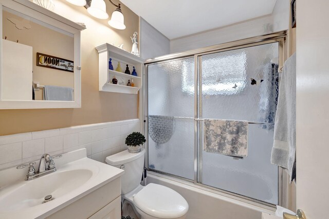 full bathroom featuring toilet, vanity, decorative backsplash, bath / shower combo with glass door, and tile walls