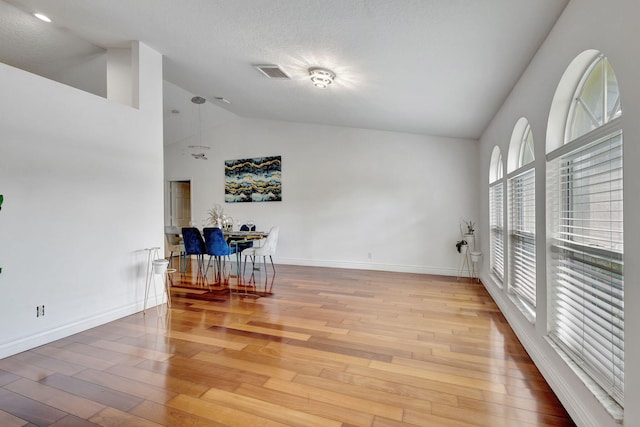 empty room featuring light wood-type flooring, a textured ceiling, and high vaulted ceiling