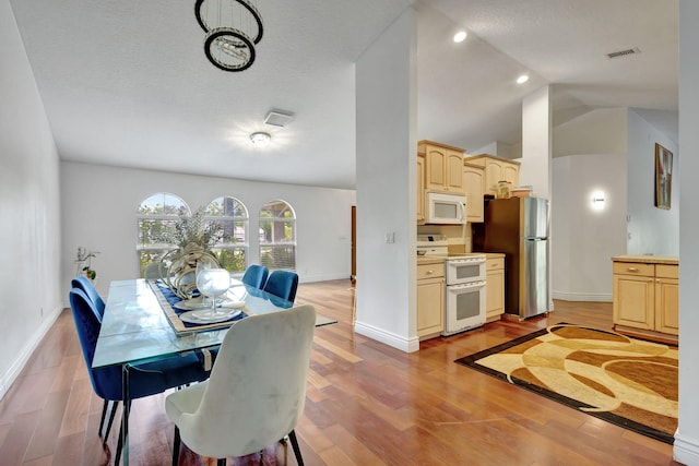 dining room with light wood-type flooring, vaulted ceiling, and a textured ceiling