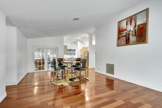 dining space featuring a textured ceiling, vaulted ceiling, and hardwood / wood-style flooring