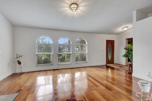 empty room featuring a textured ceiling, a healthy amount of sunlight, light wood-type flooring, and lofted ceiling