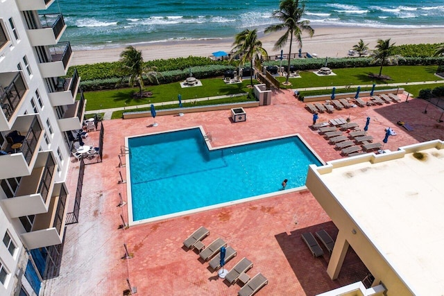 view of swimming pool featuring a view of the beach, a water view, a lawn, and a patio