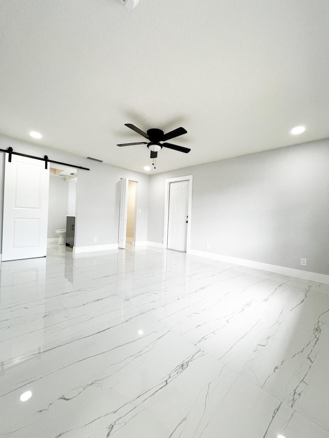 spare room with a textured ceiling, a barn door, and ceiling fan