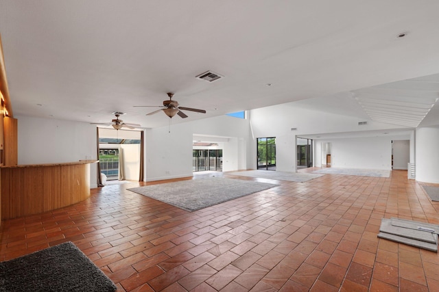 unfurnished living room with ceiling fan, brick floor, and visible vents