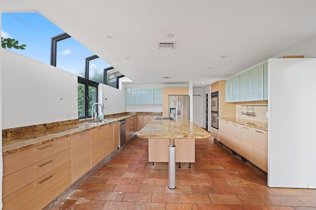 kitchen featuring appliances with stainless steel finishes, a breakfast bar, light stone countertops, light brown cabinetry, and a center island