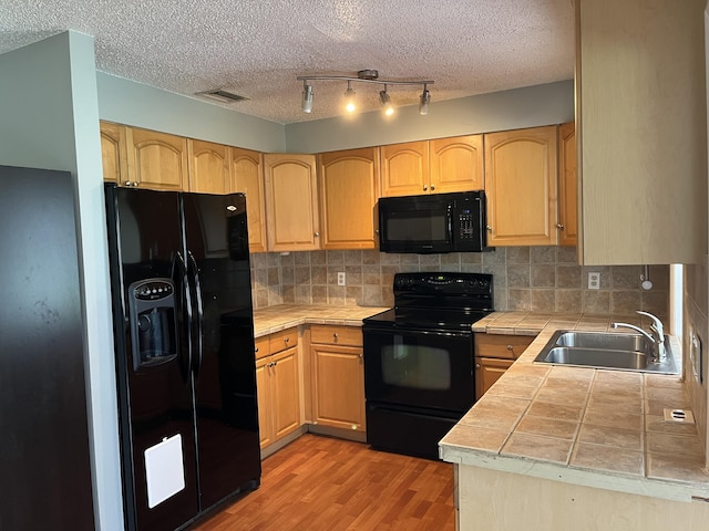 kitchen featuring tile countertops, light hardwood / wood-style floors, sink, black appliances, and a textured ceiling