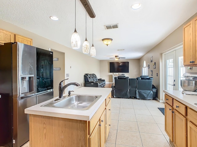 kitchen featuring hanging light fixtures, stainless steel fridge, ceiling fan, a center island with sink, and sink