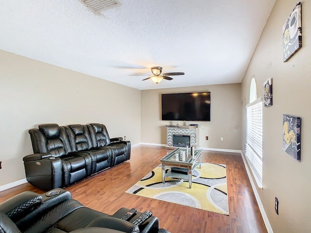 living room featuring ceiling fan, hardwood / wood-style flooring, a fireplace, and a textured ceiling