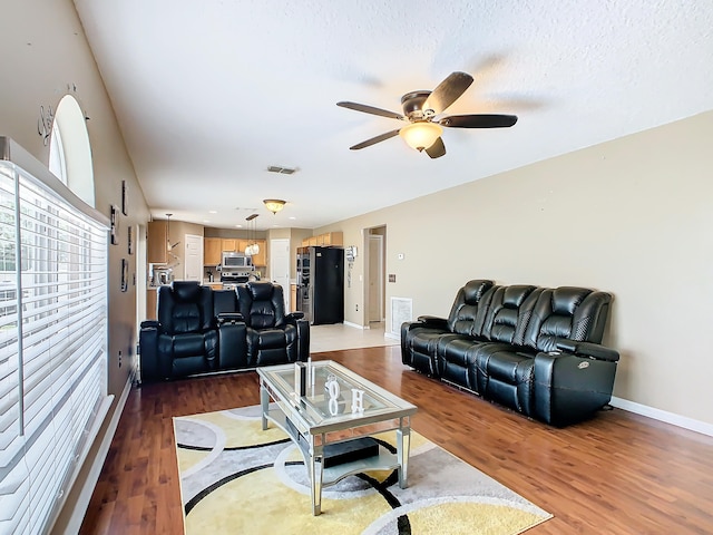 living room with light wood-type flooring, a textured ceiling, and ceiling fan