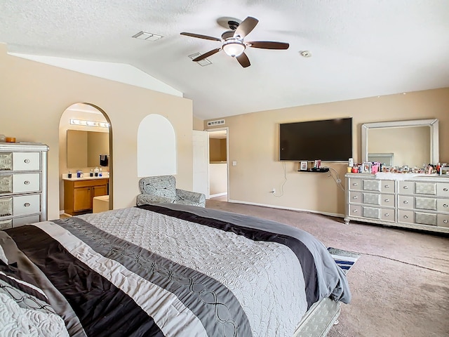 bedroom featuring a textured ceiling, vaulted ceiling, carpet floors, ensuite bath, and ceiling fan