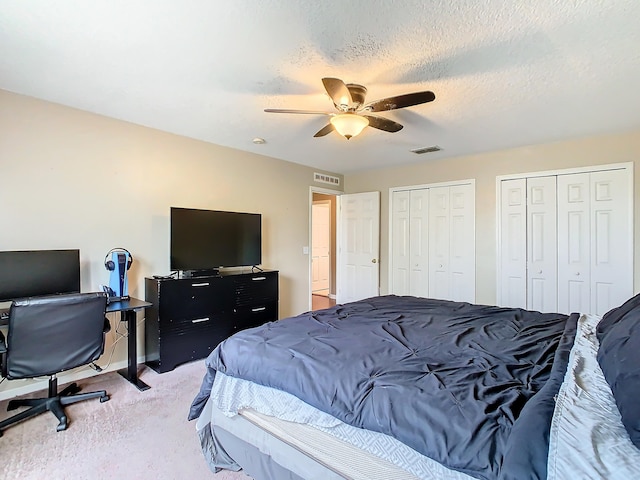 carpeted bedroom featuring a textured ceiling, two closets, and ceiling fan