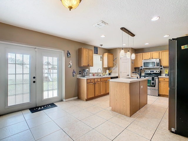 kitchen with an island with sink, hanging light fixtures, light tile patterned floors, sink, and stainless steel appliances