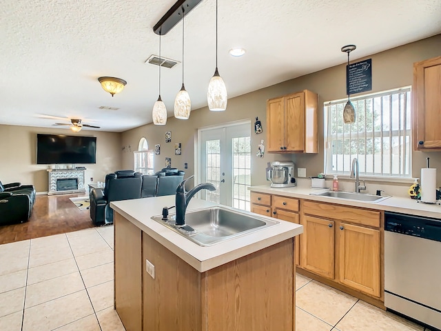 kitchen with light hardwood / wood-style floors, an island with sink, a stone fireplace, stainless steel dishwasher, and sink