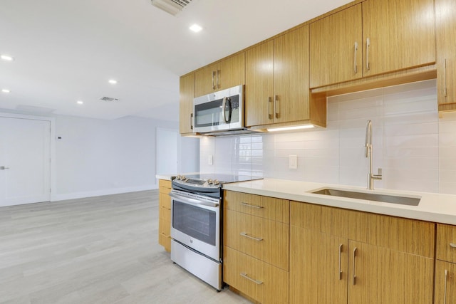 kitchen featuring appliances with stainless steel finishes, backsplash, light wood-type flooring, and sink