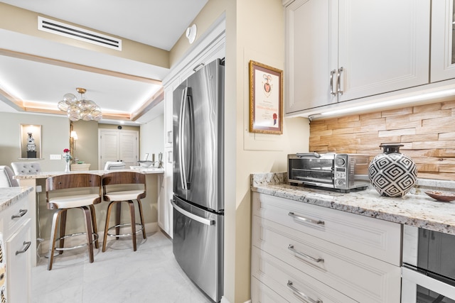 kitchen featuring backsplash, light stone counters, white cabinetry, stainless steel fridge, and a raised ceiling