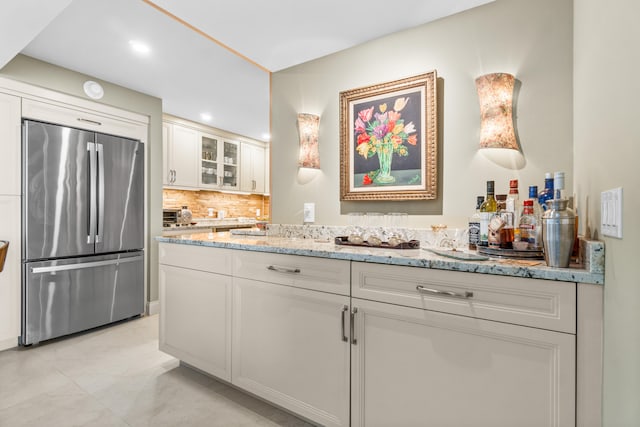 kitchen featuring white cabinetry, tasteful backsplash, light stone counters, and stainless steel refrigerator