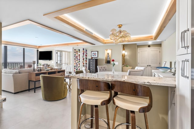 kitchen with a raised ceiling, a chandelier, light stone countertops, and a breakfast bar