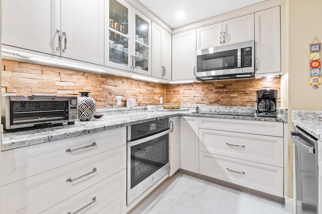 kitchen with stainless steel appliances, light stone counters, backsplash, and white cabinets