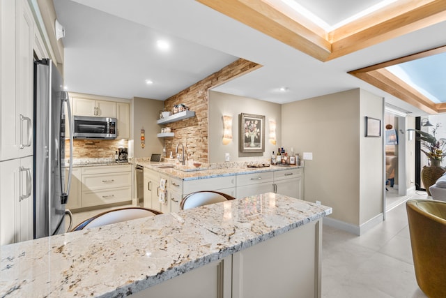 kitchen featuring stainless steel appliances, light stone countertops, kitchen peninsula, and tasteful backsplash