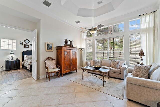 tiled living room with a textured ceiling, crown molding, a tray ceiling, and ceiling fan