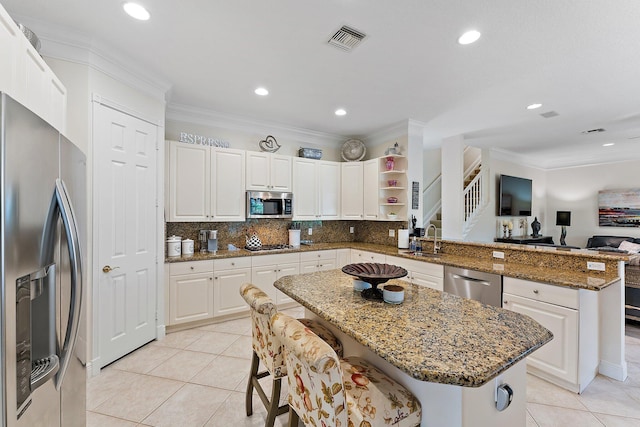 kitchen with white cabinets, sink, appliances with stainless steel finishes, a center island, and dark stone counters