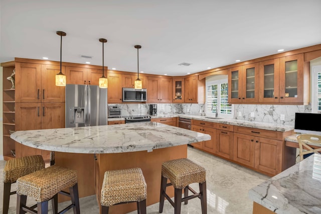 kitchen with light stone countertops, a center island, stainless steel appliances, a kitchen breakfast bar, and pendant lighting