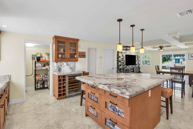 kitchen with wine cooler, ceiling fan, light stone countertops, decorative light fixtures, and a kitchen island