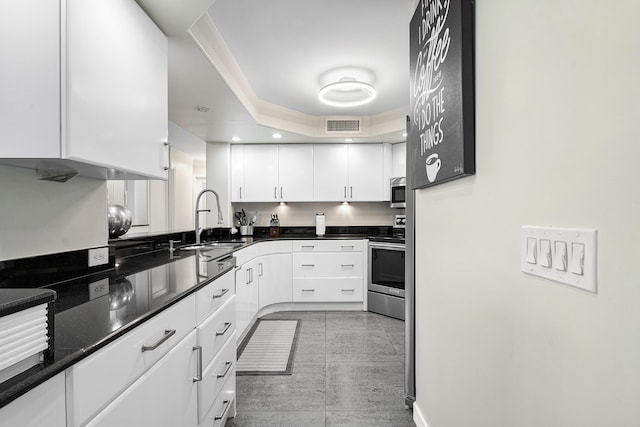 kitchen with appliances with stainless steel finishes, white cabinetry, sink, a tray ceiling, and light tile patterned flooring