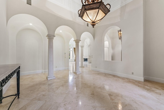 spare room with crown molding, a towering ceiling, and ornate columns