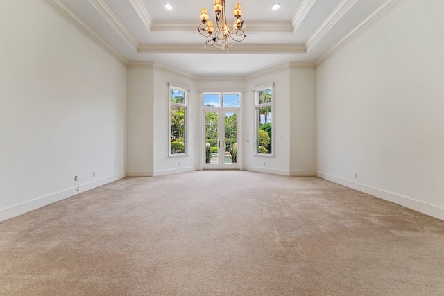 carpeted spare room with a tray ceiling, a notable chandelier, and ornamental molding