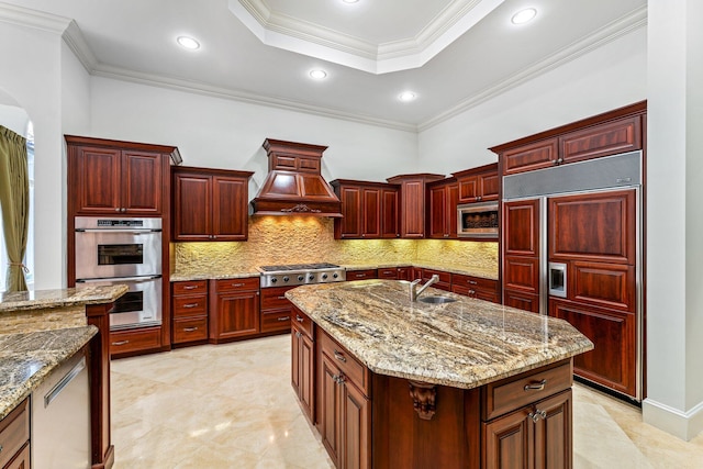 kitchen with built in appliances, tasteful backsplash, a kitchen island with sink, ornamental molding, and custom exhaust hood