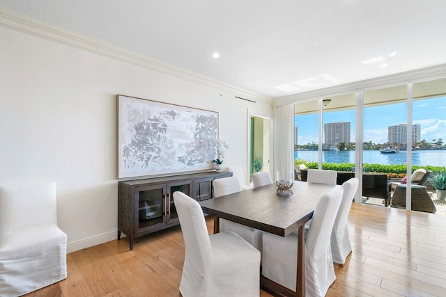 dining area featuring a wealth of natural light, a water view, ornamental molding, and light wood-type flooring