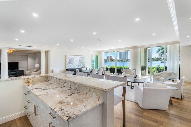 kitchen with a spacious island, light stone countertops, crown molding, and light hardwood / wood-style floors