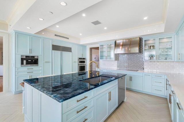 kitchen featuring decorative backsplash, appliances with stainless steel finishes, sink, wall chimney range hood, and a center island with sink