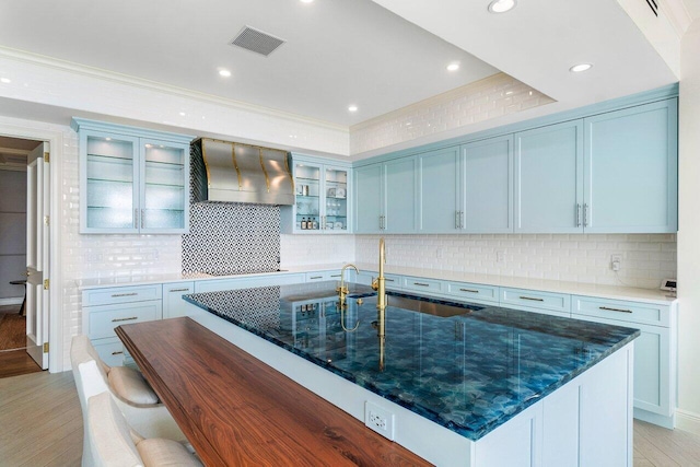 kitchen with custom range hood, tasteful backsplash, light hardwood / wood-style flooring, and dark stone countertops