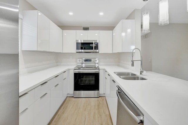 kitchen with hanging light fixtures, sink, light hardwood / wood-style flooring, white cabinetry, and stainless steel appliances