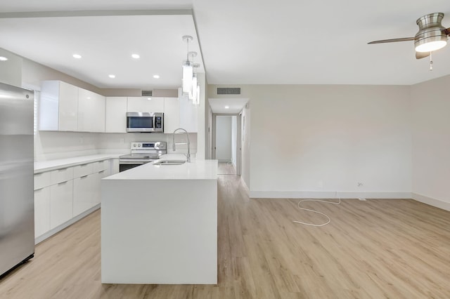 kitchen featuring light wood-type flooring, sink, white cabinetry, appliances with stainless steel finishes, and decorative light fixtures