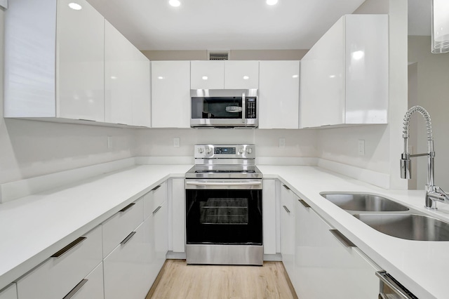 kitchen featuring appliances with stainless steel finishes, light wood-type flooring, white cabinetry, and sink