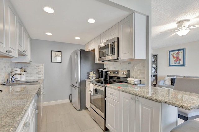 kitchen with ceiling fan, light stone counters, stainless steel appliances, and white cabinetry