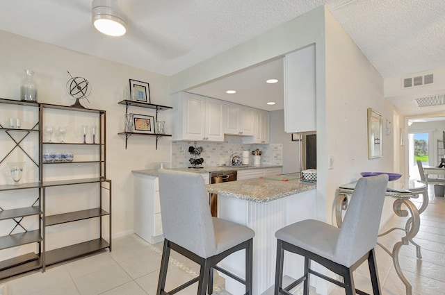 kitchen featuring a textured ceiling, a kitchen breakfast bar, kitchen peninsula, white cabinetry, and light stone counters