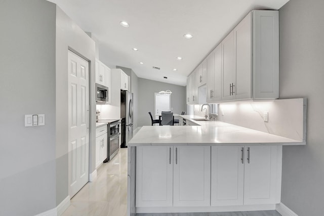 kitchen featuring appliances with stainless steel finishes, kitchen peninsula, sink, white cabinetry, and lofted ceiling