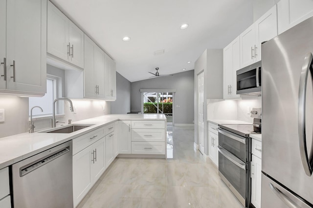 kitchen featuring vaulted ceiling, appliances with stainless steel finishes, kitchen peninsula, sink, and white cabinetry